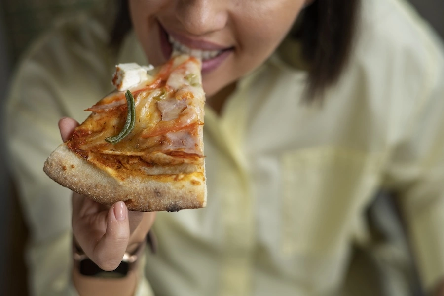 Femme dégustant une part de pizza artisanale Augusto Pizza, solution snacking présentée au Salon Alpin d'Albertville pour l'hôtellerie