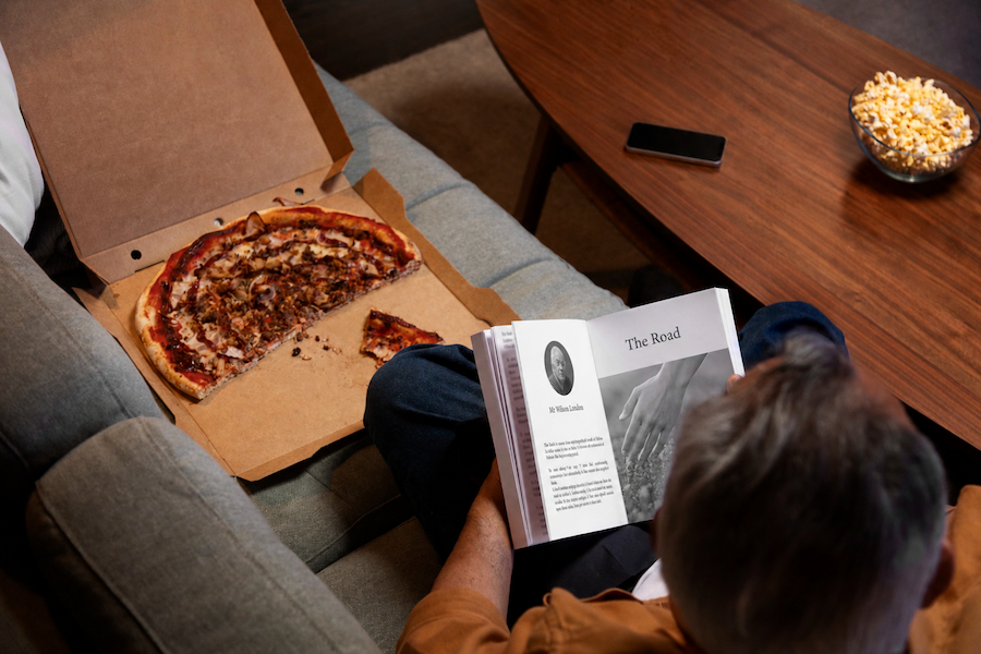 Personne dégustant une pizza à l’hôtel en lisant un livre, illustration d'une soirée détente autour d'un moment de snacking