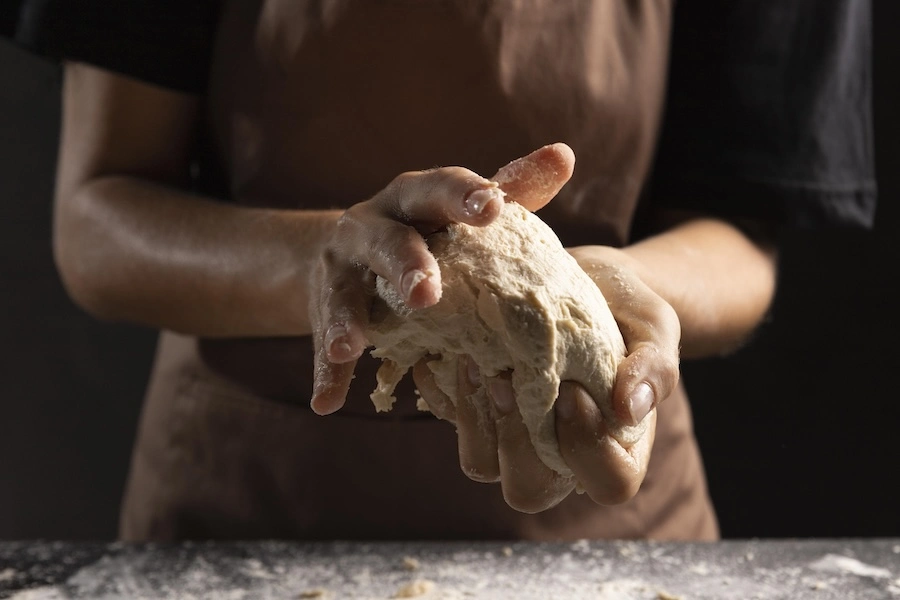 Chef pétrissant à la main une pâte à pizza artisanale, illustration du savoir-faire de fabrication professionnel Augusto Pizza