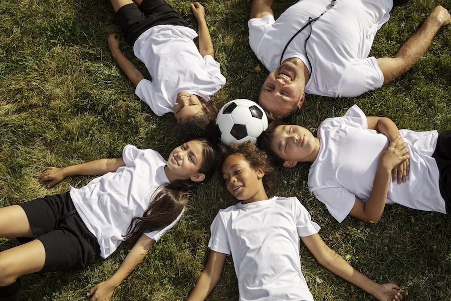 Plusieurs enfants allongés sur le sol avec un ballon de foot au milieu