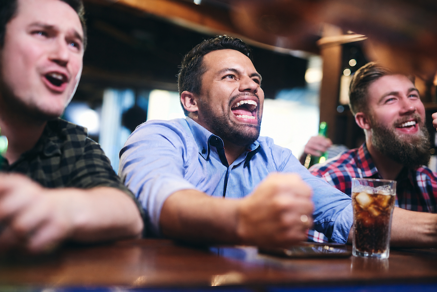 Groupe de clients enthousiastes regardant une retransmission sportive dans un bar à bières