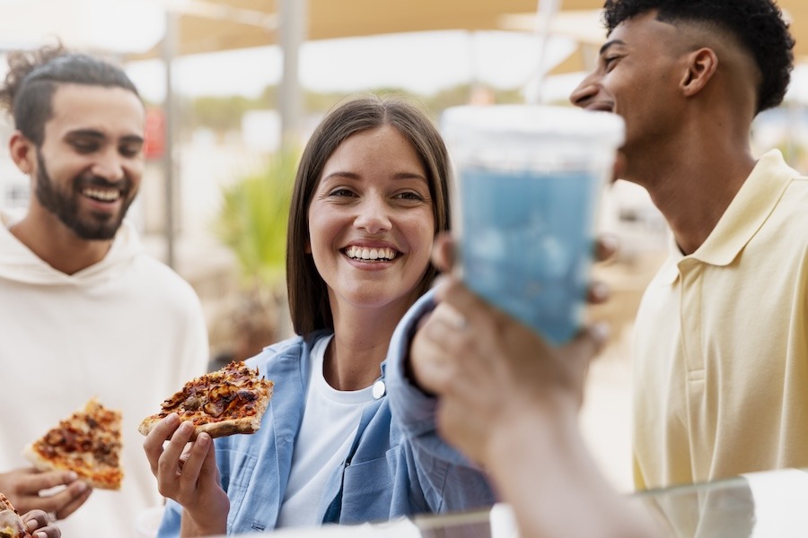 Amis en pause sur la route des vacances partageant des parts de pizza en station-service, illustration d'une offre snacking adaptée aux trajets estivaux