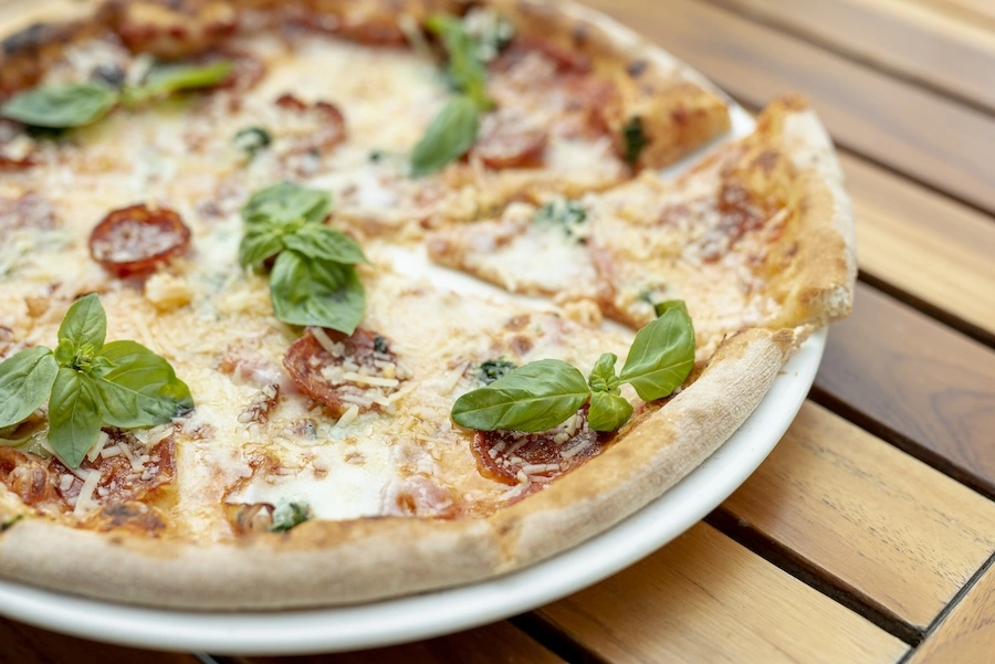 Pizza artisanale garnie de tomates, chorizo et basilic frais, servie sur une table en bois, illustrant une offre de snacking clé en main sans personnel dédié