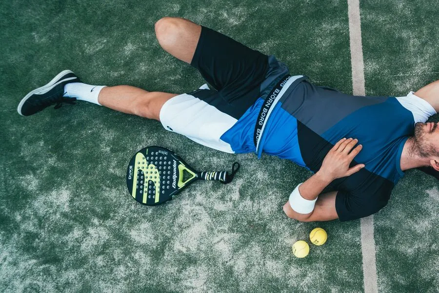 Vue du dessus d'un joueur de padel qui récupère au sol en fin de match, raquette et deux balles près de lui